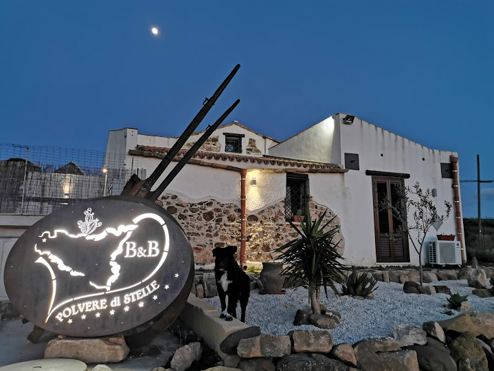 B&B Polvere di Stelleの石造りの建物。明かりのついた看板と、その前にいる犬。