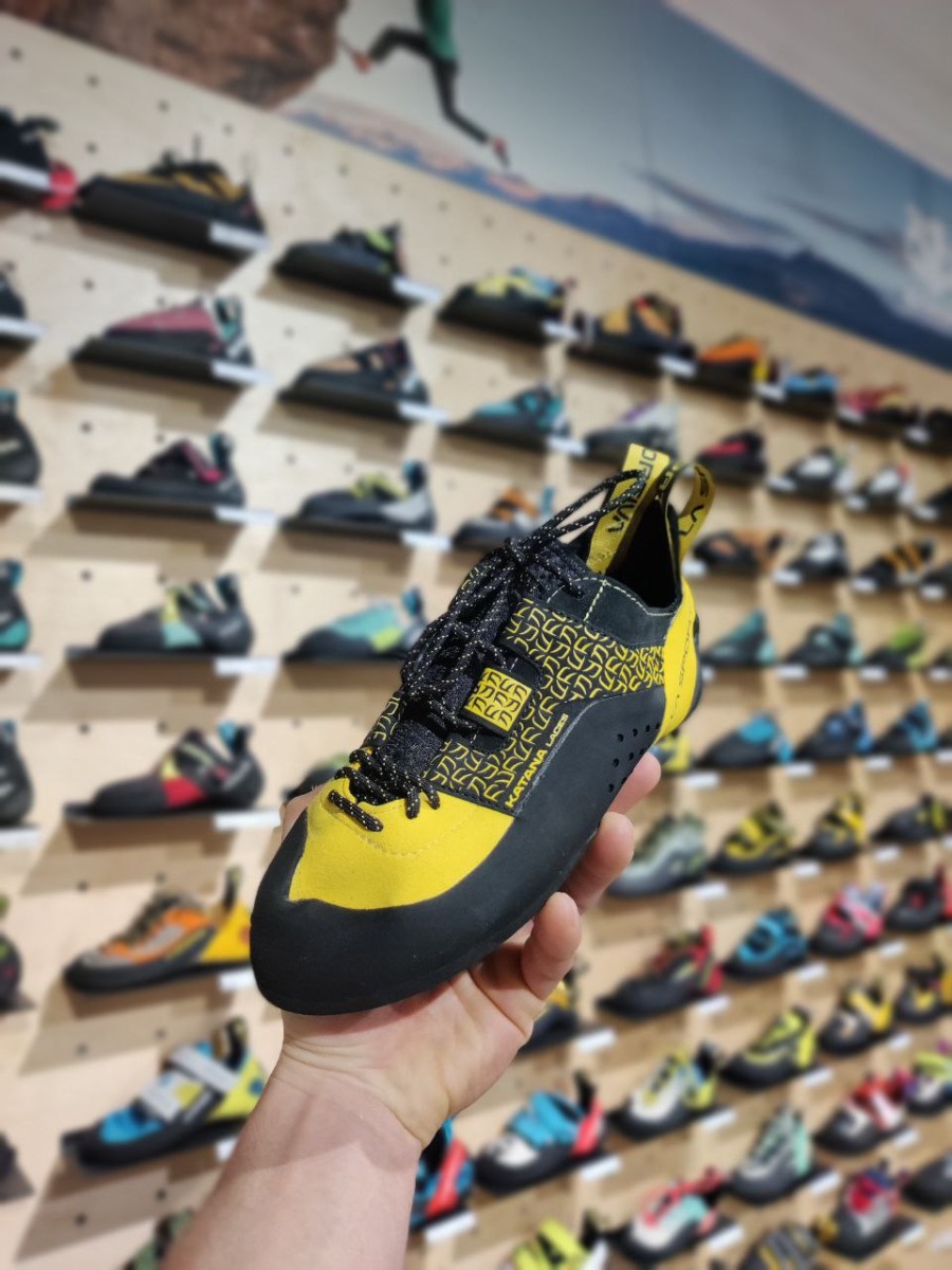 シューズの展示を背景に、黄色と黒のレースアップシューズを持つ手