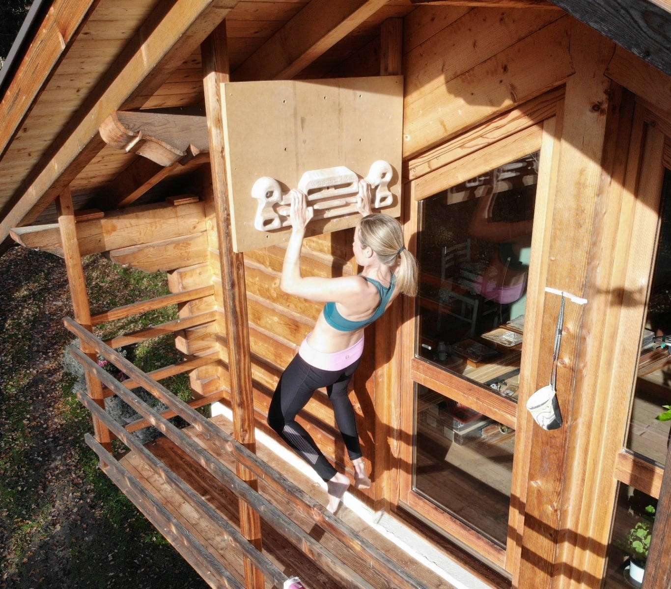 木造の建物の外側のパネルに取り付けたWoodoClimbのハングボードでトレーニングする人