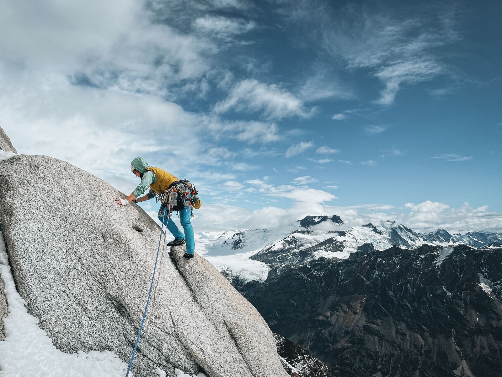 雪山を背景に、ハーネスとロープを使って岩を登る人物 — Alexa Flower, Patagonia