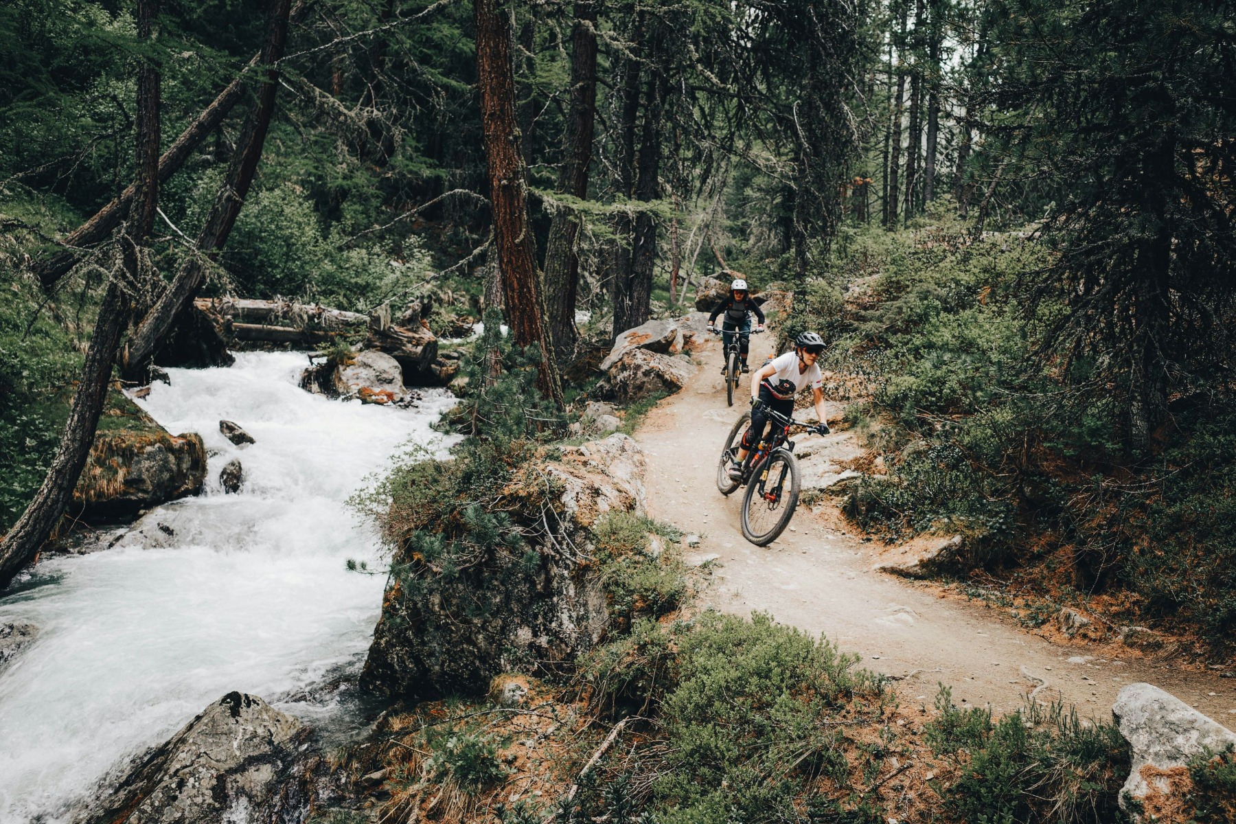 小川沿いの森の道でマウンテンバイクに乗るふたり — Graziano De Maio Unsplash
