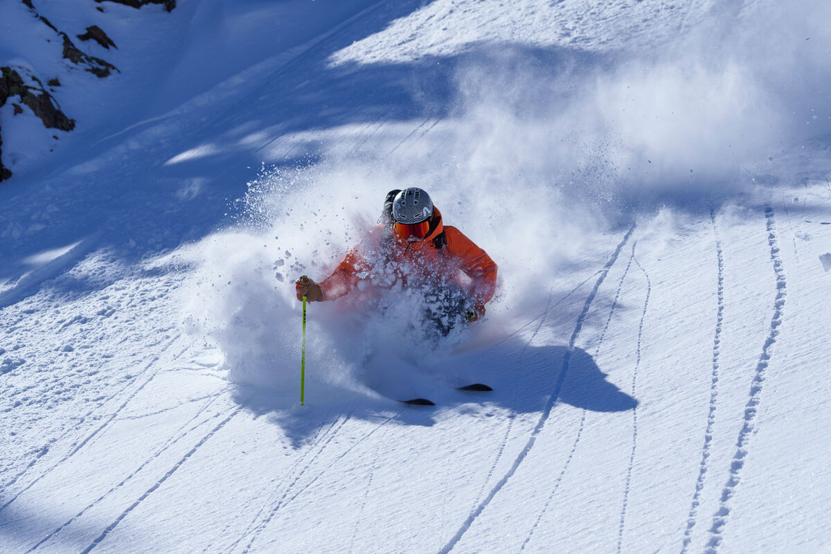 ヘルメットとオレンジ色のジャケットを着用した人が、粉雪を舞い上げながら滑る