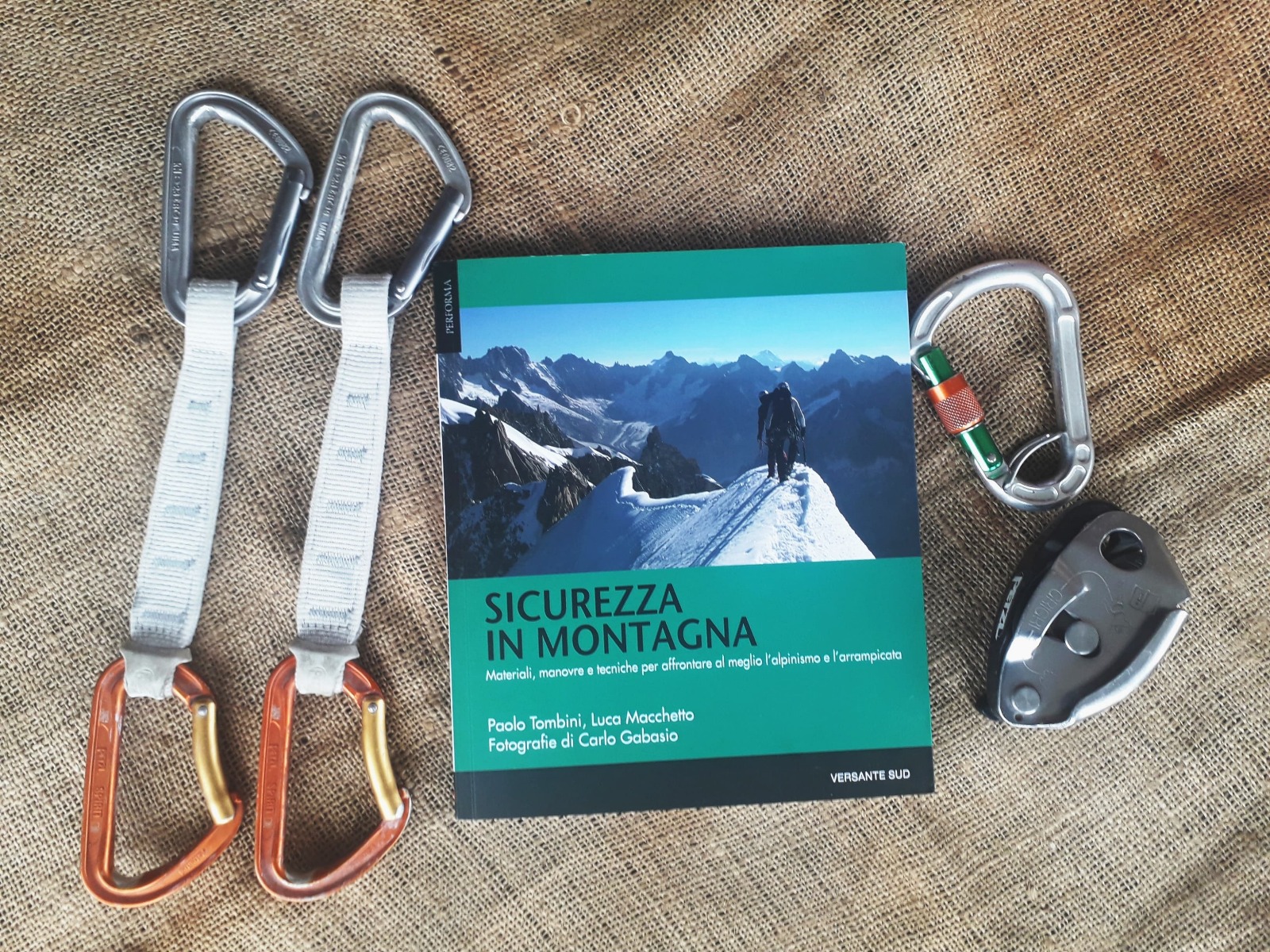 Sicurezza in Montagnaのイタリア語版の表紙。隣にはクイックドロー二本、ロック式カラビナ、ビレイデバイスが置かれている