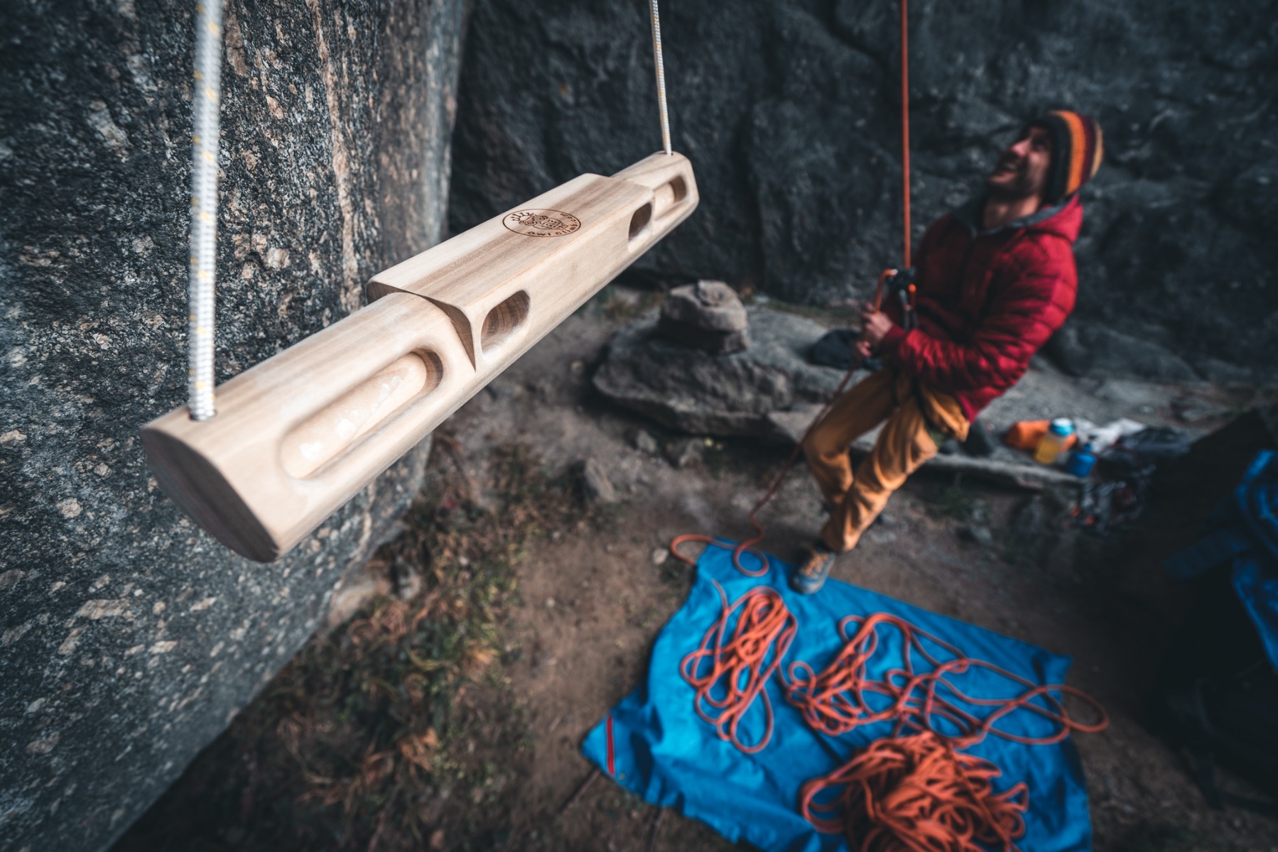 岩の近くに吊るされた木製の携帯型ハングボードOwl Climb Portable。背景には人とロープが見える。