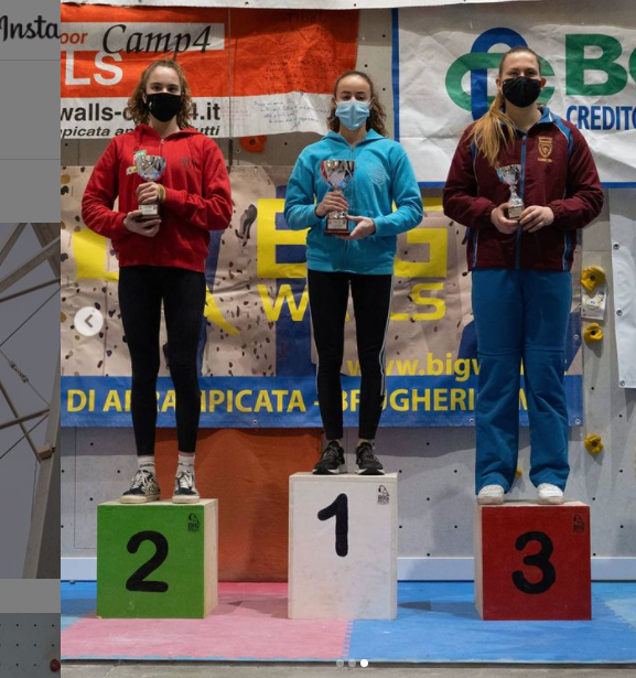 クライミング壁の前の表彰台に立ち、マスクを着けてカップを持つ3人の選手。