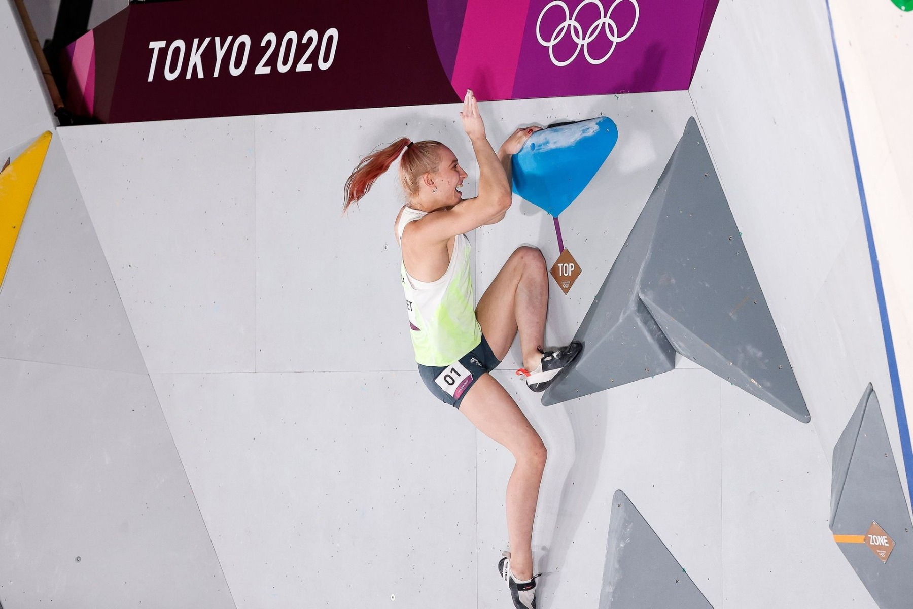 IFSC 東京2020でトップホールドに片手を置き、もう一方の手を上げる女子クライマー