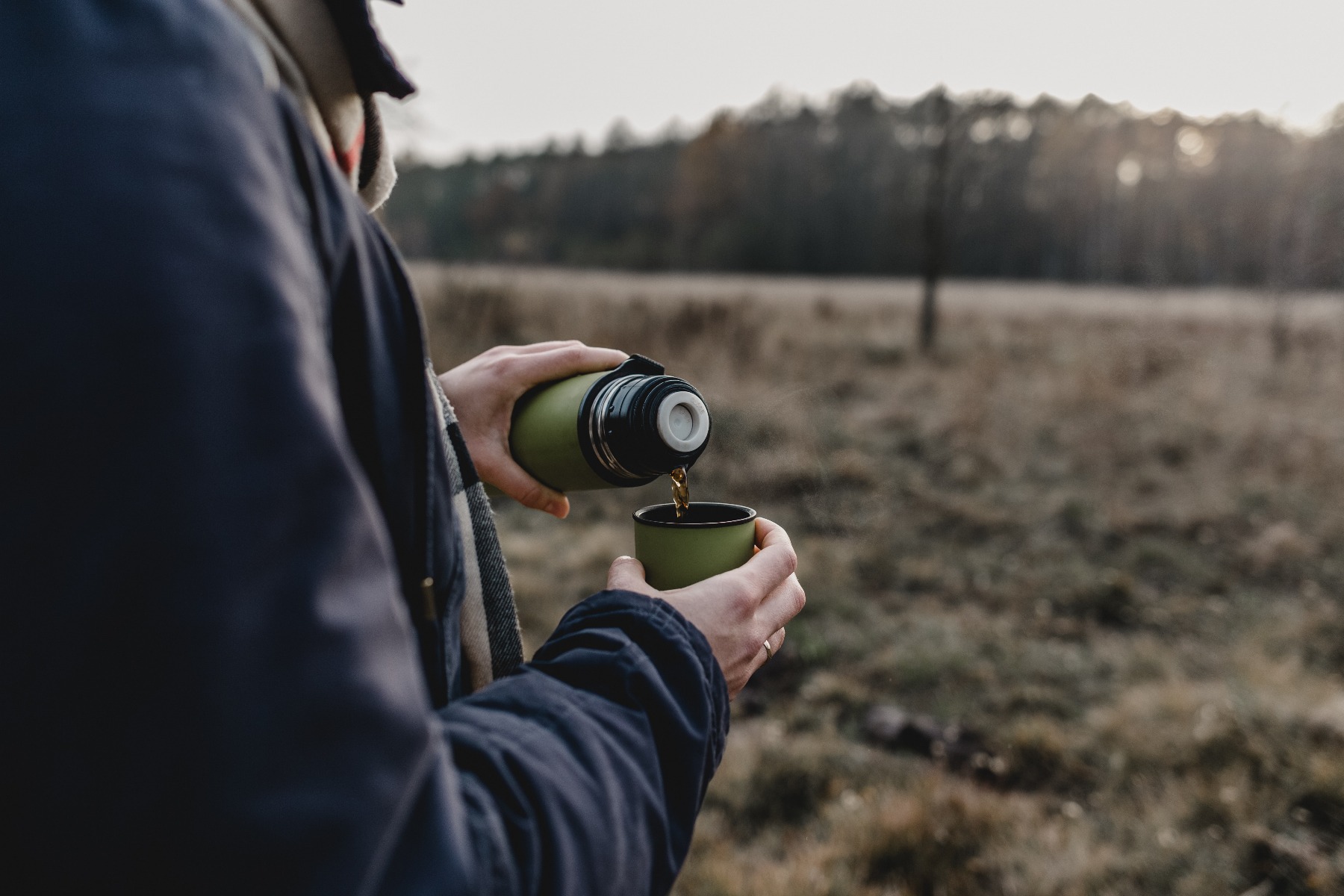 Kamil Szum from Unsplash 屋外で、保温ボトルからカップに飲み物を注ぐ人。