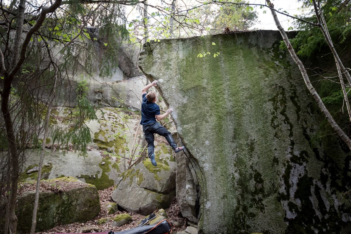 森の苔のある大きな岩を登るクライマー。撮影:Tristan Hobson、SCARPA