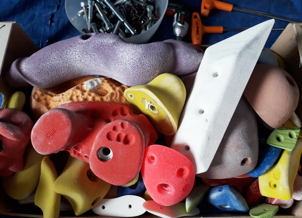 lavare le prese, big up climbing さまざまな色のクライミングホールドが入った箱。背景にボルトや工具が見える