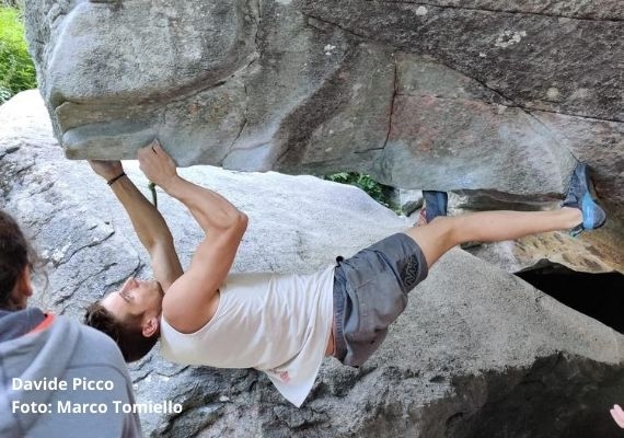 davide picco bouldering magic wood 白い袖なしのシャツ、灰色のショートパンツ、水色のクライミングシューズを着けた人が、灰色の岩のルーフの下にいる。