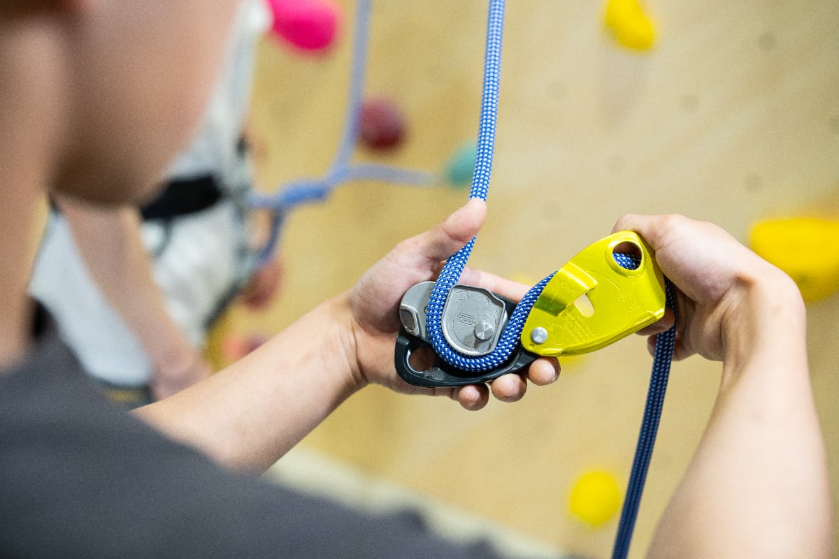 屋内のクライミングウォールで、黄色いPetzl GriGri+に青いロープを通す手元