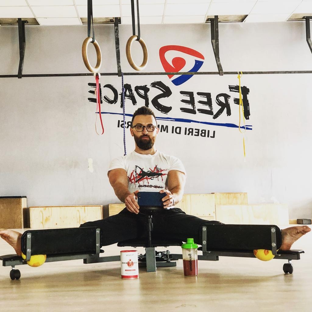 Daniel Destefanis ジムの器具に脚を開いて座る、眼鏡と明るい色のTシャツを着用した人物