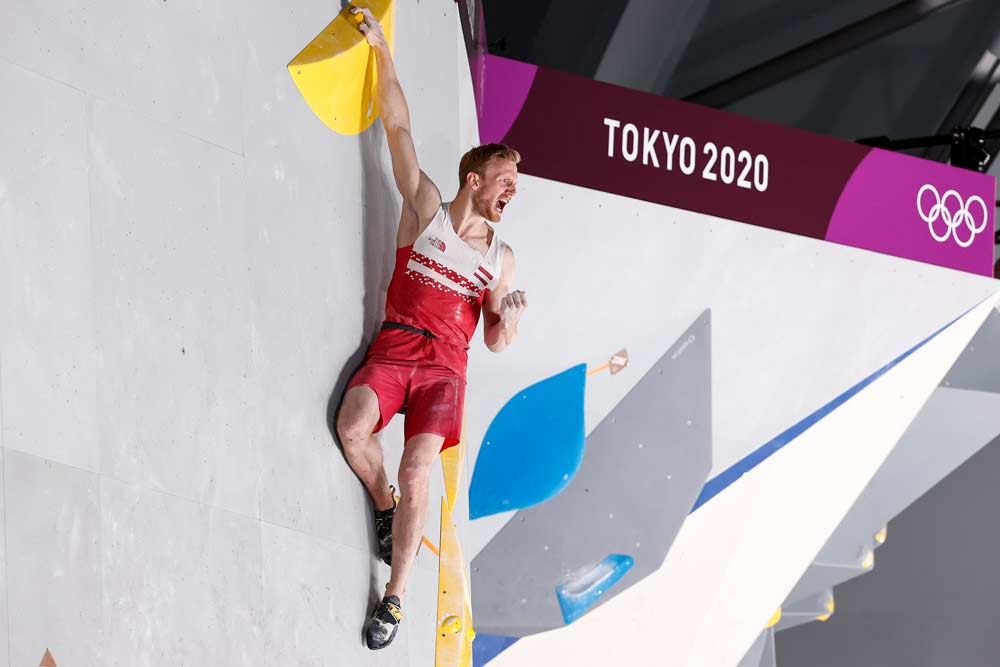 Tokyo 2020のボルダー壁で黄色いホールドに片手を置いて喜ぶJakob Schubert