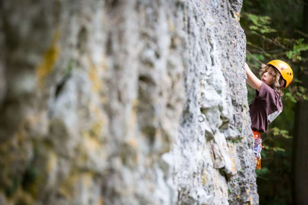 Fonte: petzl.com caschetti arrampicata bimbi 黄色いヘルメットとハーネスを着け、岩壁を登る若いクライマー