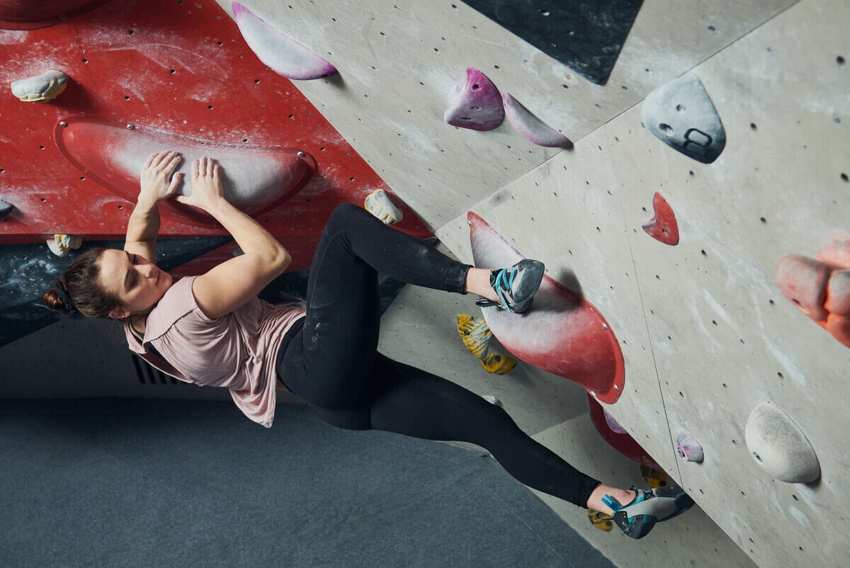 屋内ボルダー壁の大きなホールドを登るクライマー。写真:Ray Demski、SCARPA