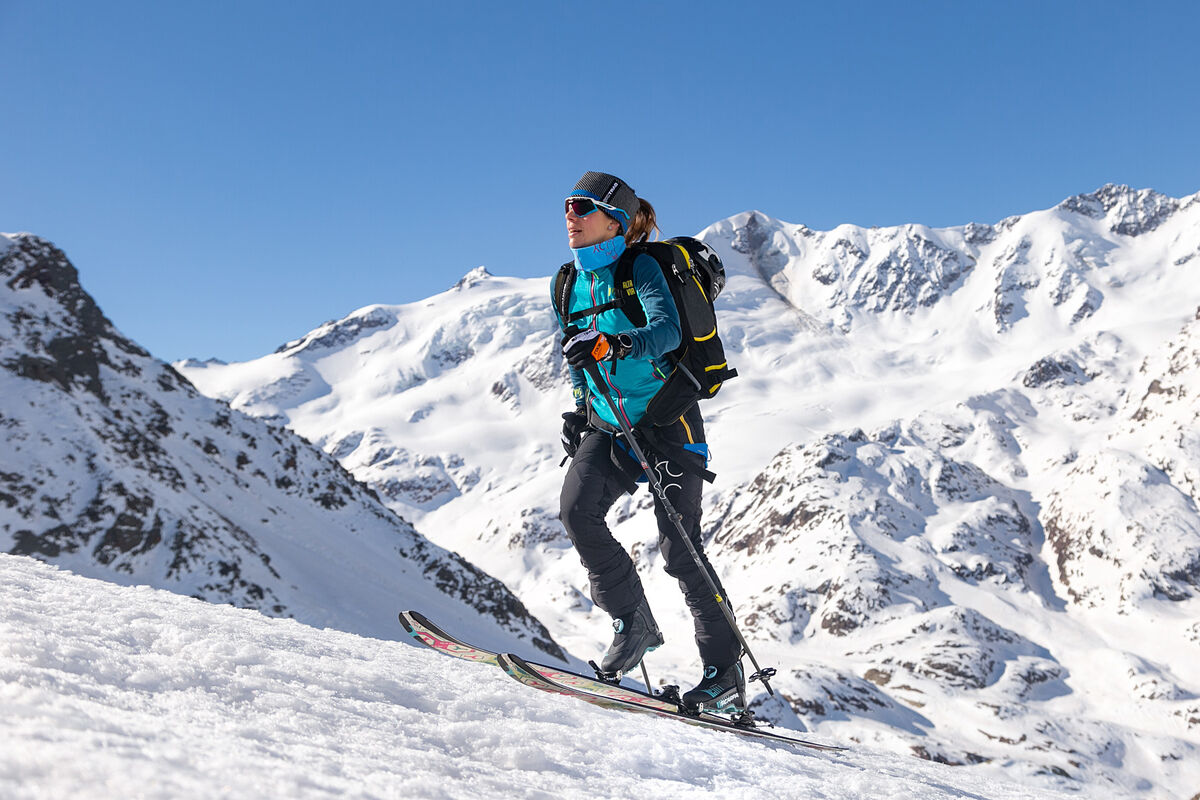 山の雪の斜面に、スキー、ストック、バックパックを持った人がいる