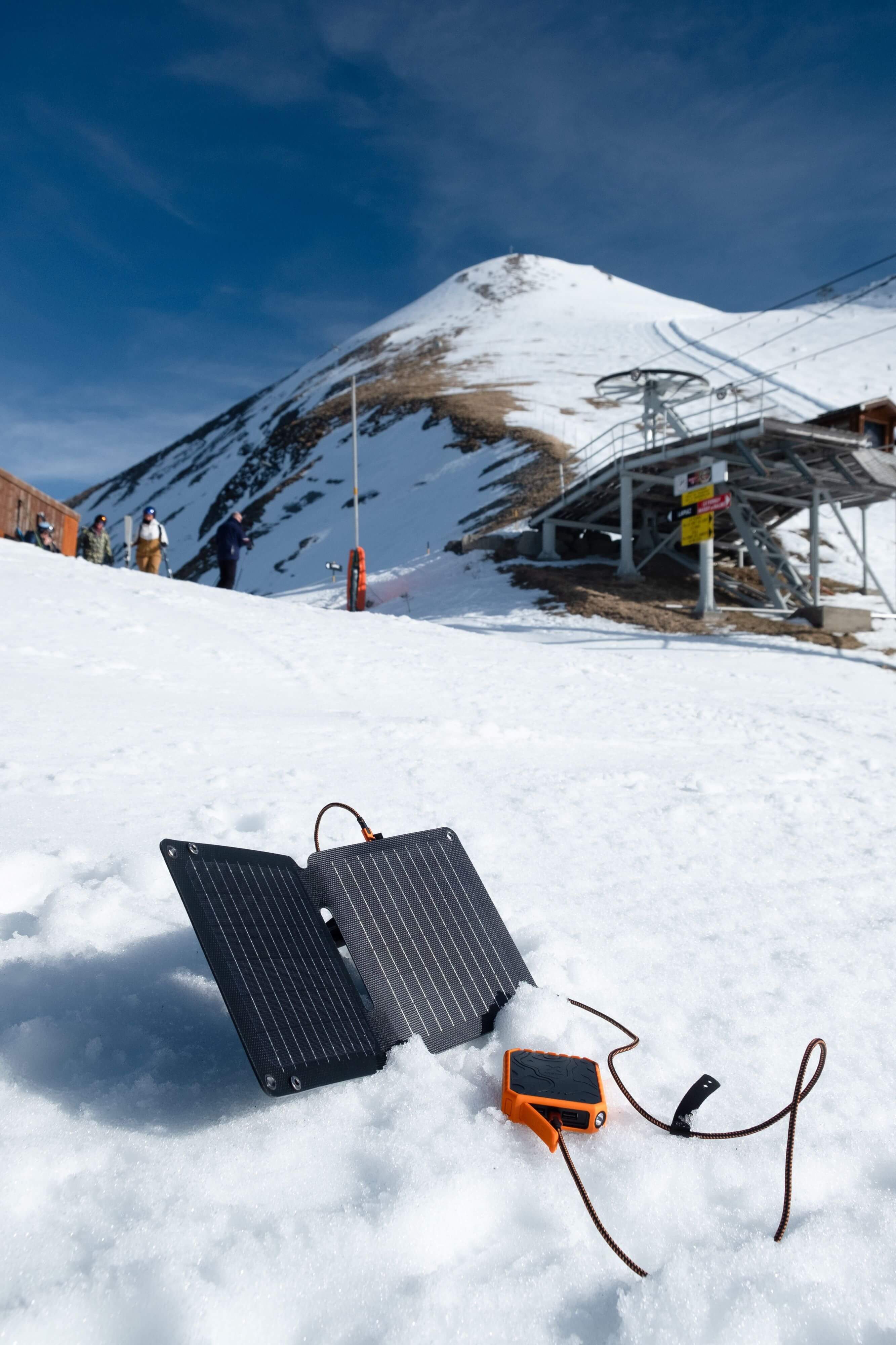 雪の上に置かれた折りたたみ式Xtorm SolarBoosterとオレンジのモバイルバッテリー