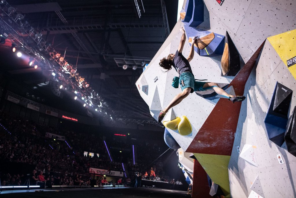 credits adidasrockstars.com 観客のいるアリーナで、大きな色付きのボリュームがあるボルダリング壁を登る人 — credits adidasrockstars.com