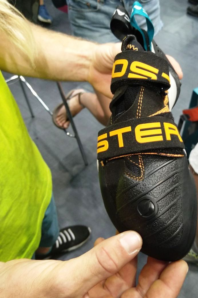 Scarpa Booster S 黄色い帯と二つの面ファスナーが付いた黒いクライミングシューズを手で持っている