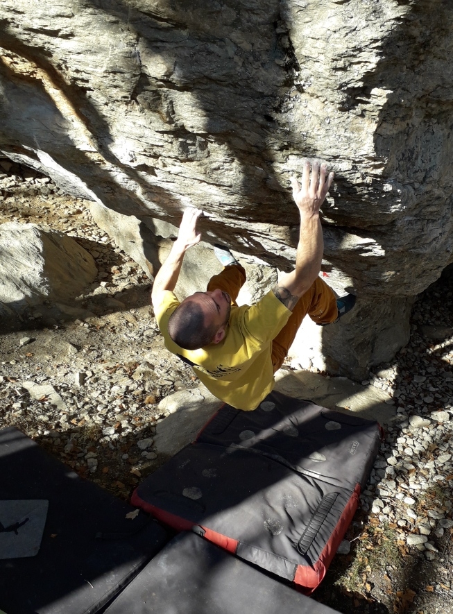 bouldering a valdinferno 赤い縁の黒いクラッシュパッドの上で、黄色いTシャツを着た人が岩を登っている