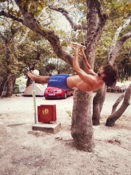 fornt lever su Portable di Owl Climb, Stefano Montecucco 木々の間の木製トレーニング器具に、体を水平にしてぶら下がる人