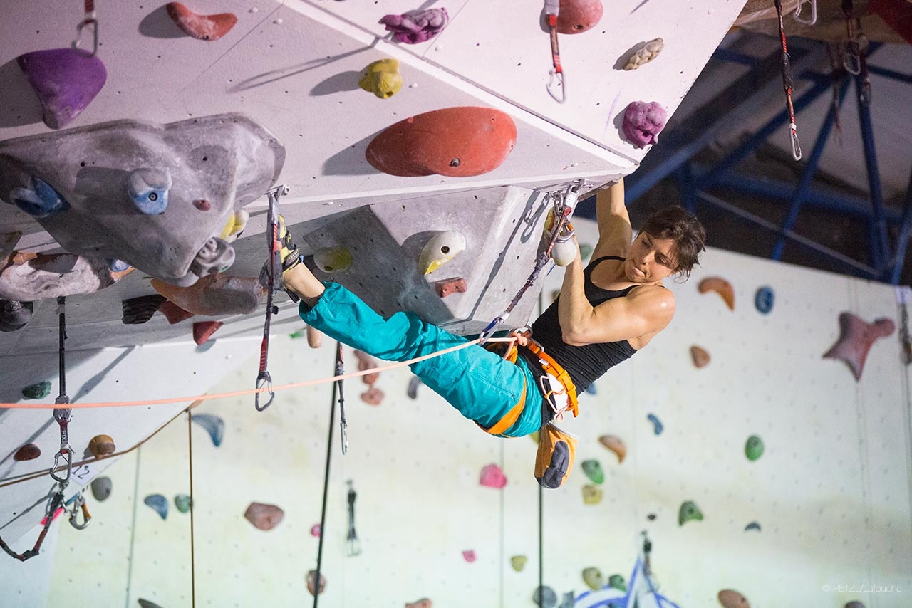 indoor climbing, fonte petzl.com Labouche ロープとハーネスを着用し、カラフルなホールドがある屋内の前傾壁を登る人
