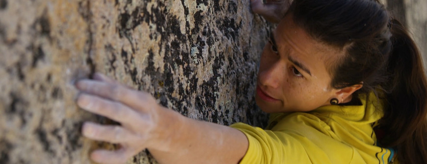 Nina Williams, photo credits: www.eoft.eu 黄色いトップスを着て、岩壁に片手を添えるクライマー — Nina williams, photo credits: www.eoft.eu