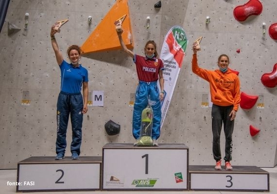 2020年イタリア・リードクライミング選手権の女子表彰台 屋内クライミング壁の前にある番号付きの表彰台で、トロフィーを掲げる3人。1人は青いシャツ、1人は赤い上着、1人はオレンジ色のパーカーを着用