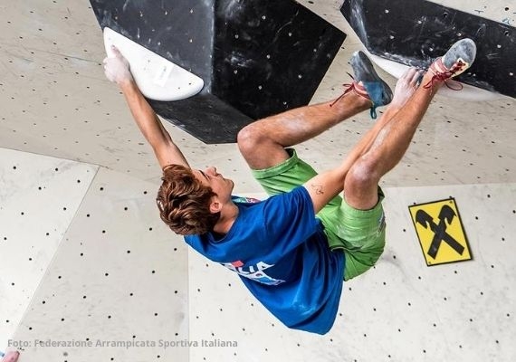 Arcoでの2020年U16ボルダー・Lead・Speed合宿 黒いボリュームと白いホールドのある人工クライミングウォールにいる、青いTシャツと薄緑色のショートパンツを着た人物。
