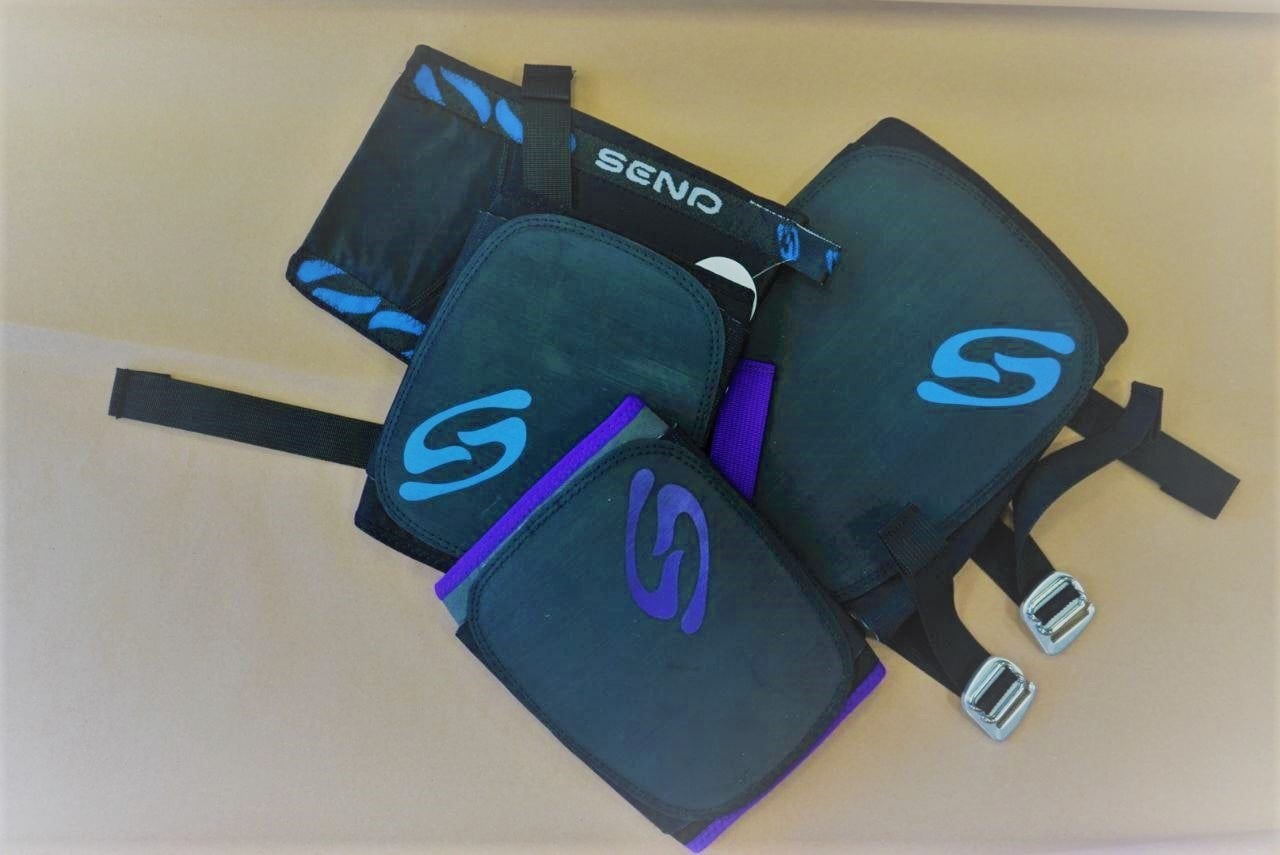 send climbing kneepad ベージュの面に置かれた、青と紫のロゴ、ストラップ、バックル付きの濃い色のニーパッド